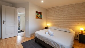 Une chambre à coucher avec une tête de lit en bois, un lit recouvert de draps blancs, deux lampes de chevet et une porte donnant sur une autre pièce.