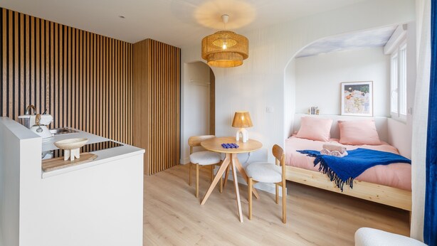 A modern, compact living space with a kitchenette, a dining area, and a cozy bedroom with a bed and pillows.