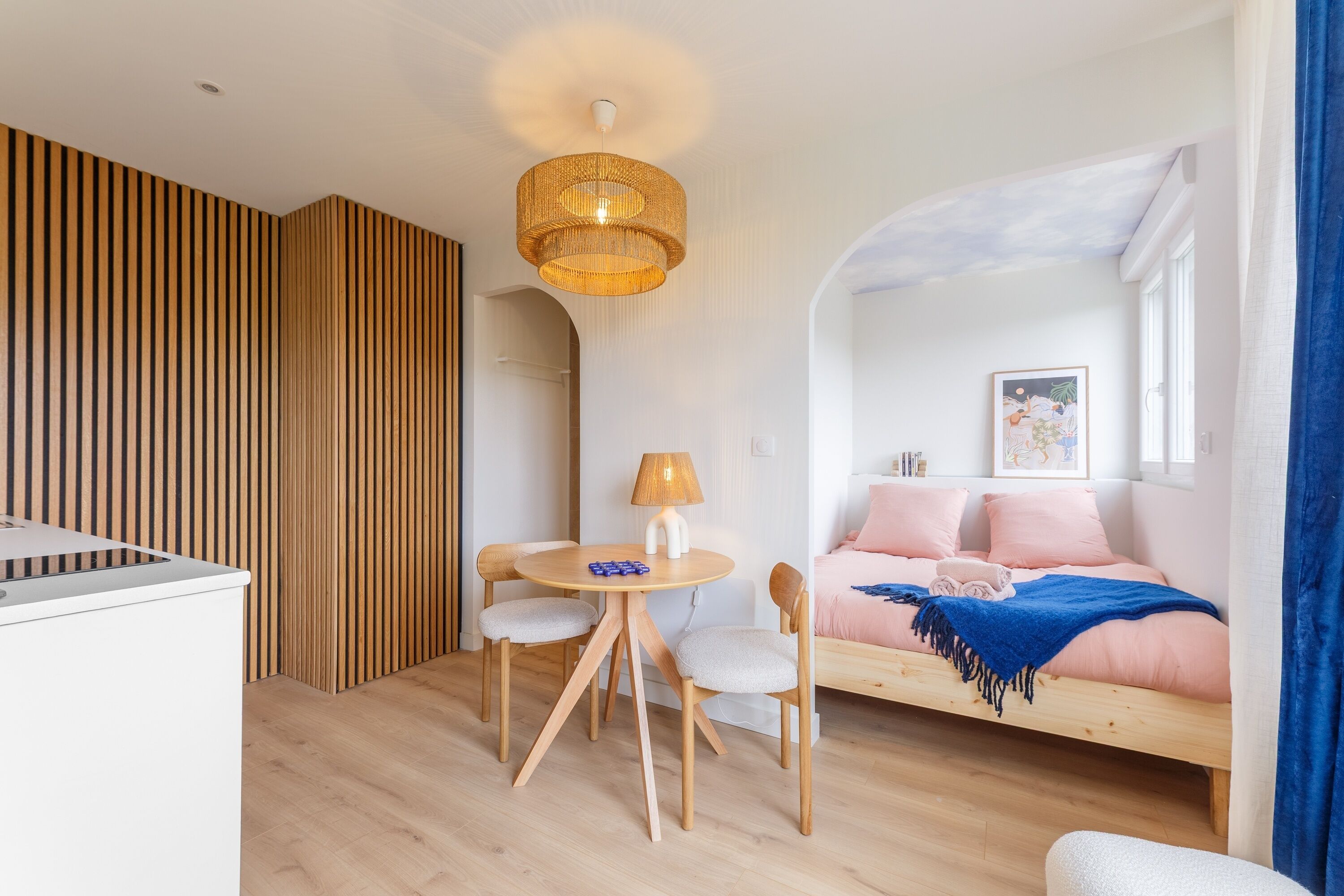 Una sala de estar moderna con piso de madera, una mesa redonda de madera con sillas, un sofá y una lámpara colgante.