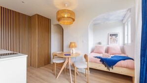 A modern living room with a wooden floor, a round wooden table with chairs, a sofa, and a hanging light fixture.