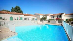A swimming pool with a tiled deck, surrounded by buildings with red-tiled roofs and white walls.