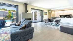A modern living room with a grey sofa, a dining area with a table and chairs, and a kitchen in the background.