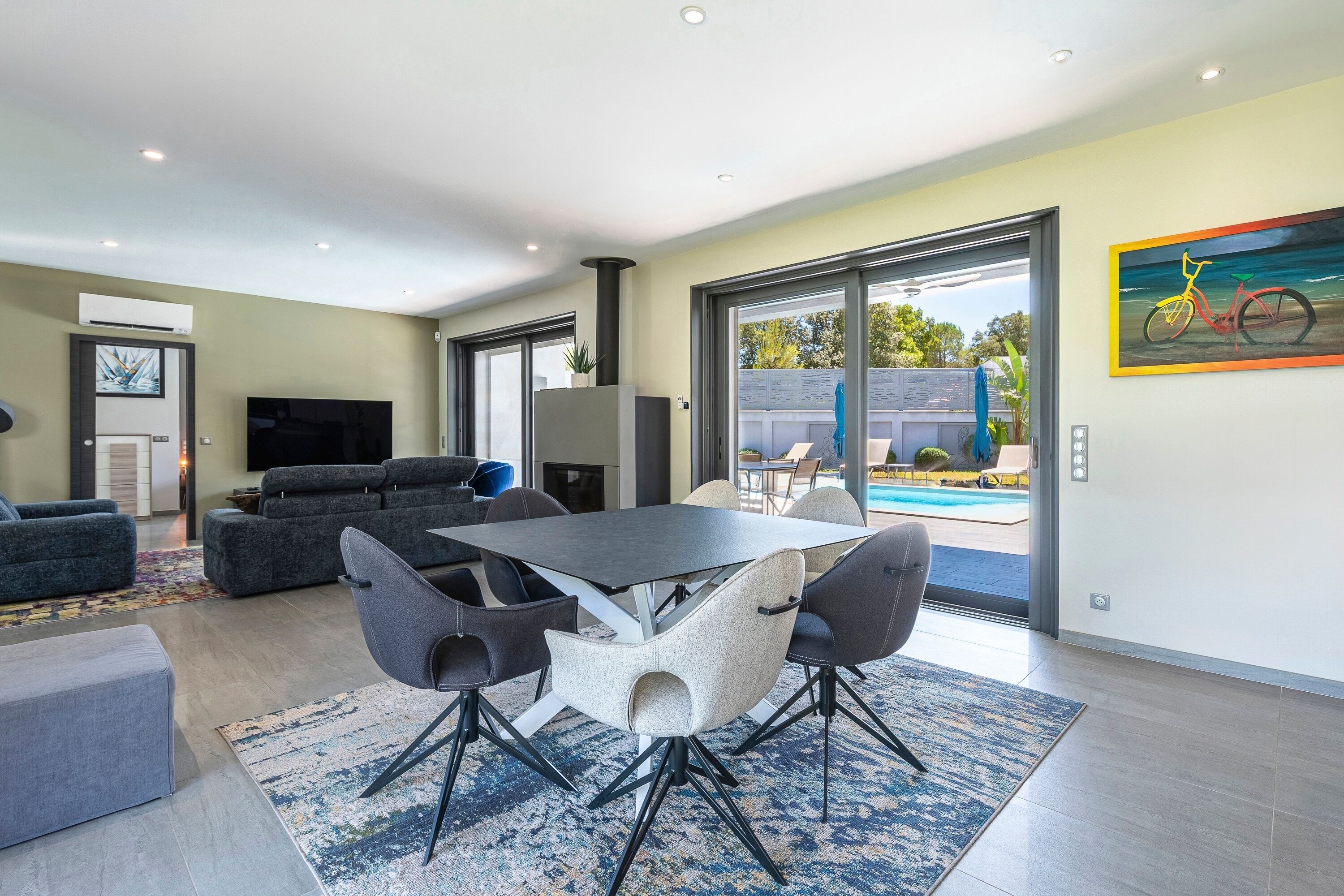 A modern living room with a dining area, a flat-screen TV, and a large sliding glass door leading to a pool.