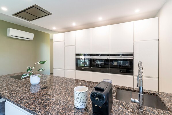 A modern kitchen with granite countertops, a coffee maker, a mug, and a sink with a modern faucet.