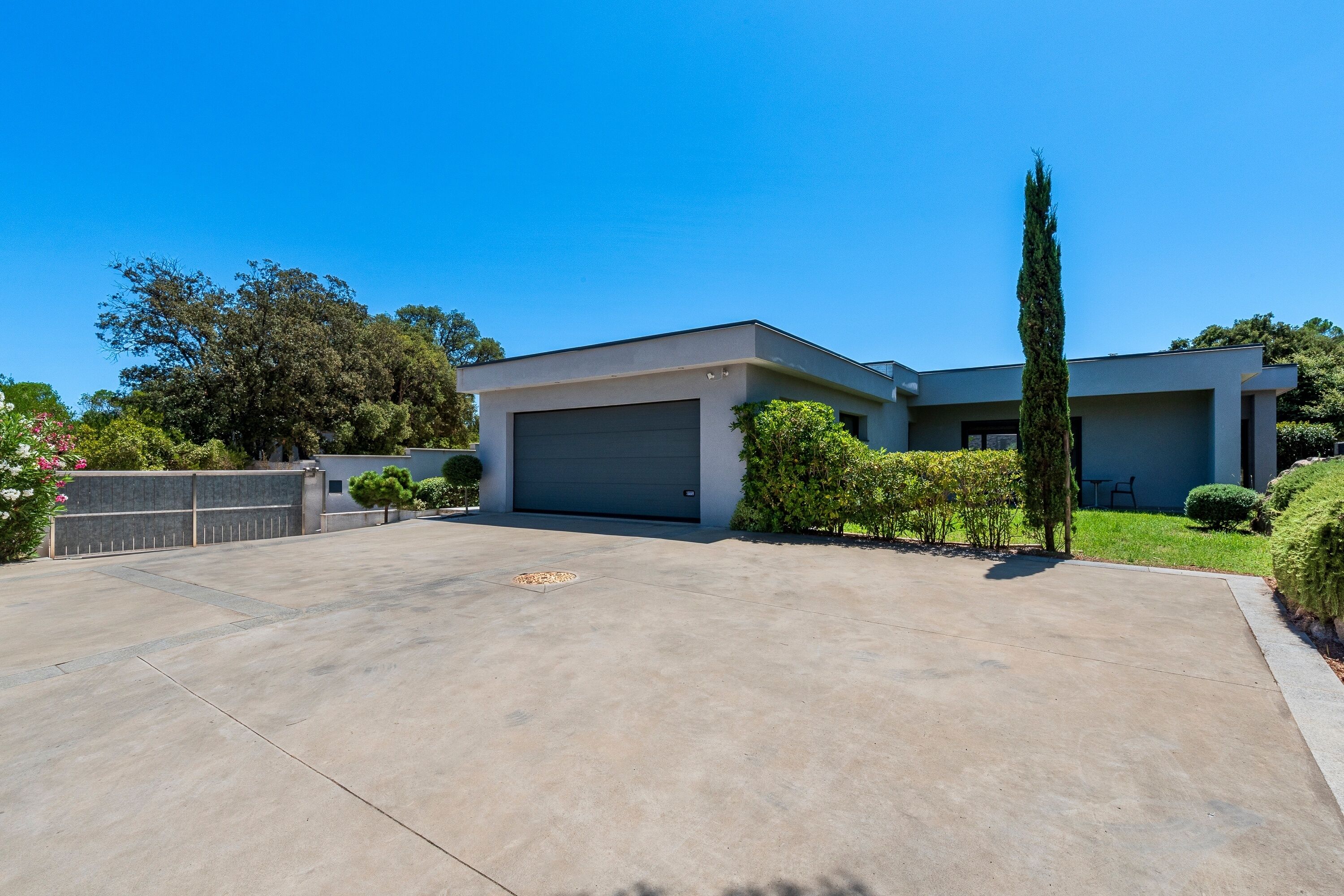 Une maison moderne à deux étages, dotée d’un grand garage, d’une pelouse bien entretenue et d’un grand cyprès.