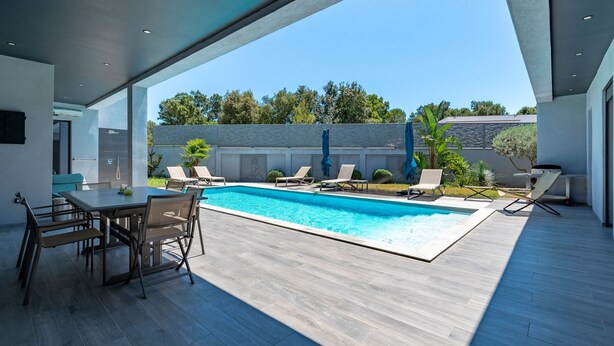 A modern outdoor pool area with a dining table and chairs, surrounded by lounge chairs.
