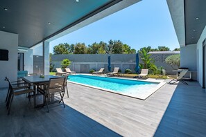 A modern outdoor pool area with a dining table and chairs, surrounded by lounge chairs.