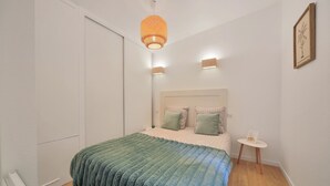 A bedroom with a bed, bedside lamps, a small table with a picture, and a ceiling light. - Les Charmes C24B - Le Val Joly (Eppe-Sauvage)