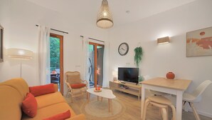 A modern living room with a sofa, a dining table, a TV, and a staircase leading to an outdoor area. - Les Charmes C24B - Le Val Joly (Eppe-Sauvage)