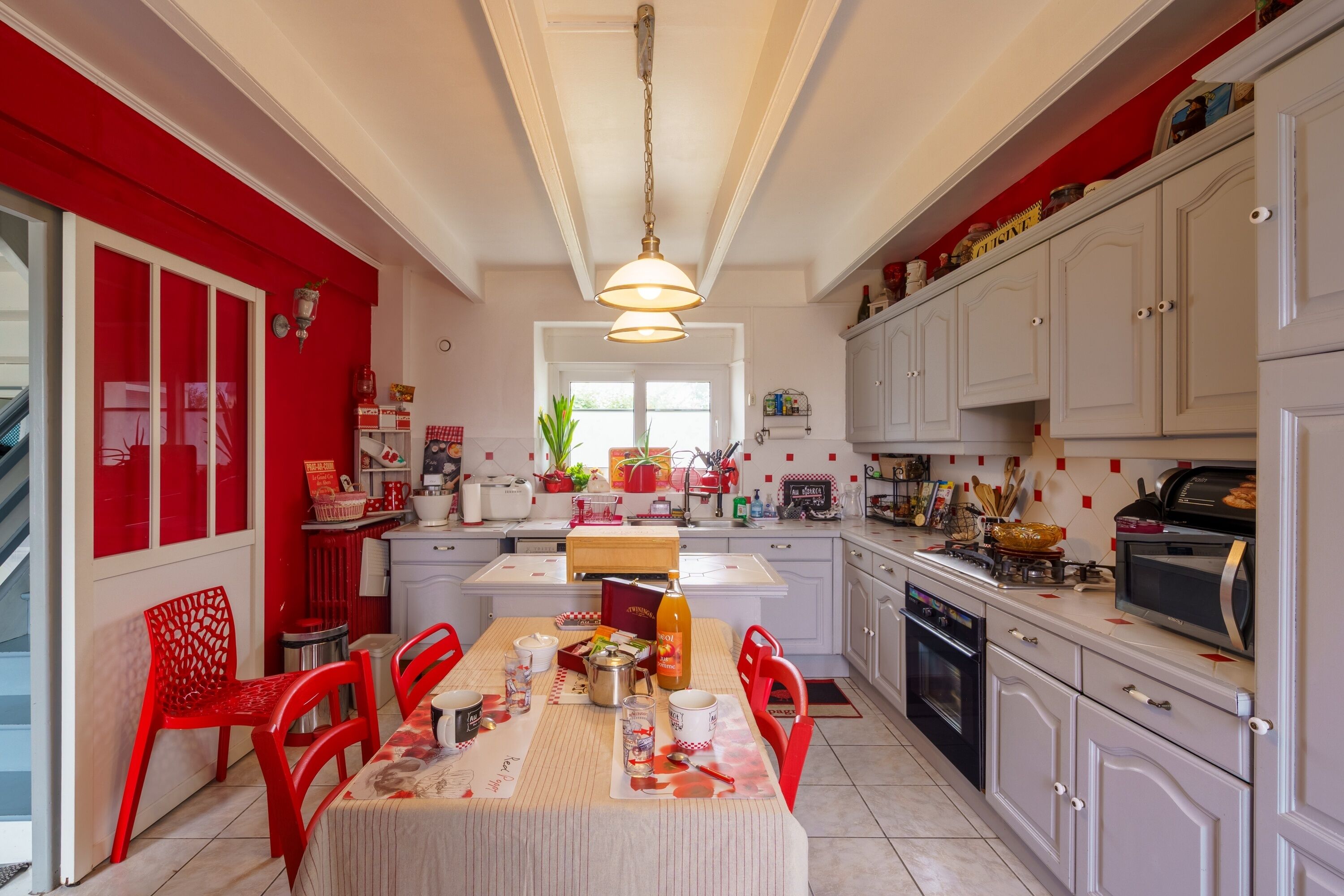 A kitchen with white cabinets, a red chair, a dining table, and a hanging light fixture.