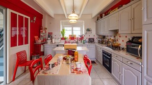 A kitchen with white cabinets, a red chair, a dining table, and a hanging light fixture.