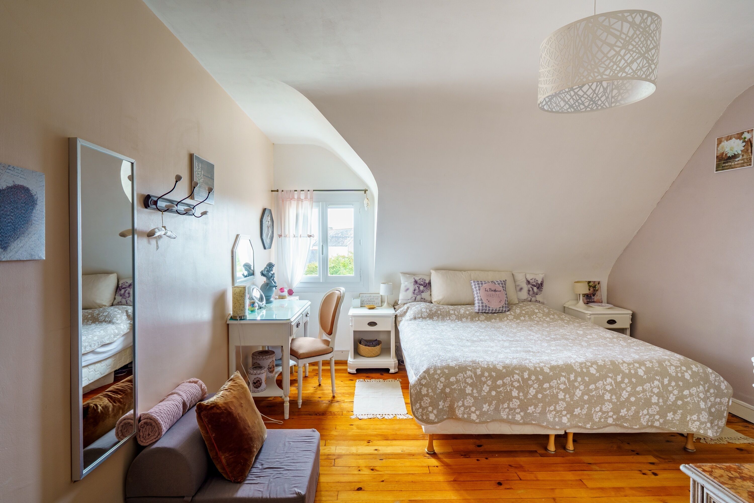 Une chambre à coucher comprenant un lit, un bureau, une chaise, un miroir et un luminaire suspendu.