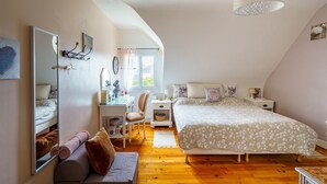 A bedroom with a bed, a desk, a chair, a mirror, and a hanging light fixture.