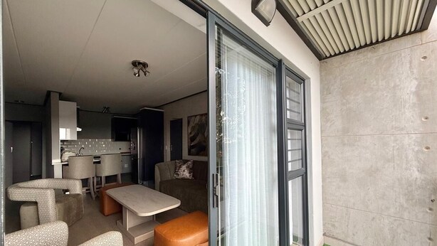 Ein modernes Interieur mit Essbereich, einer Couch und einer Schiebetür zu einem Balkon mit künstlichem Rasen.