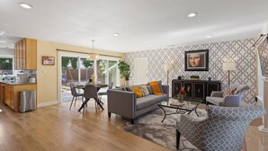 Un salon spacieux avec un canapé gris, un fauteuil à motifs et un coin repas comprenant une petite table et des chaises.