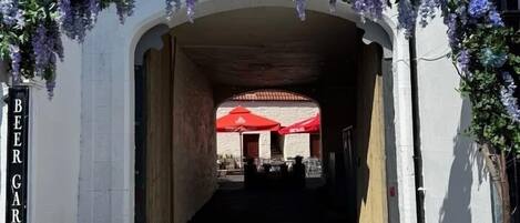 Una entrada a un jardín interior con flores moradas colgantes y un letrero arriba.