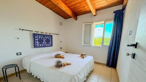Un dormitorio con cama, un taburete pequeño, una ventana con cortinas e imagen enmarcada en la pared.