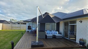 Um terraço com mobiliário externo, churrasqueira e área de estar coberta.