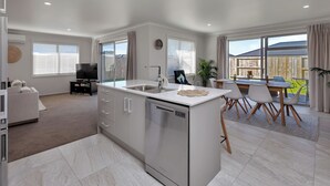 Cozinha moderna com lava-louças, área de jantar com mesa e cadeiras, e sala de estar com sofá.