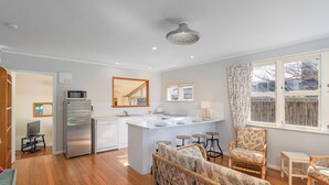 Een moderne keuken met een centraal eiland, een zithoek met rieten meubels en uitzicht op buiten door een raam.