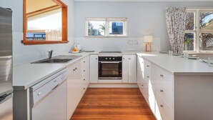 Een moderne keuken met witte kasten, een houten vloer, een inbouwoven, een spoelbak en een raam met uitzicht.