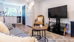 Una sala de estar moderna con un sofá, una mesa de centro, un televisor y una cocina con refrigerador y armarios.