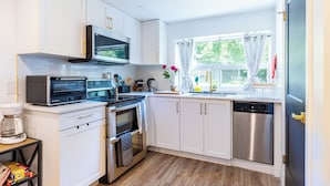 Una cocina moderna con armarios blancos, electrodomésticos de acero inoxidable y un ventanal con cortinas.