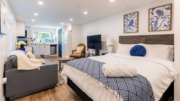 Un dormitorio moderno con una cama grande, un sofá, un televisor y una cocina al fondo.
