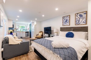 Een moderne slaapkamer met een groot bed, een bank, een televisie en een keuken op de achtergrond.
