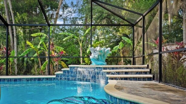 A swimming pool with a glass enclosure, surrounded by tropical plants and a decorative fountain. - Oasis privacy heated Pool Game room 3 mins Sister Spring (Crystal River)
