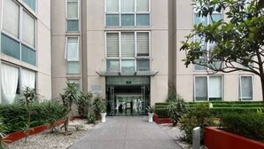 Un edificio moderno con una entrada central, rodeado de áreas ajardinadas con árboles y arbustos pequeños.