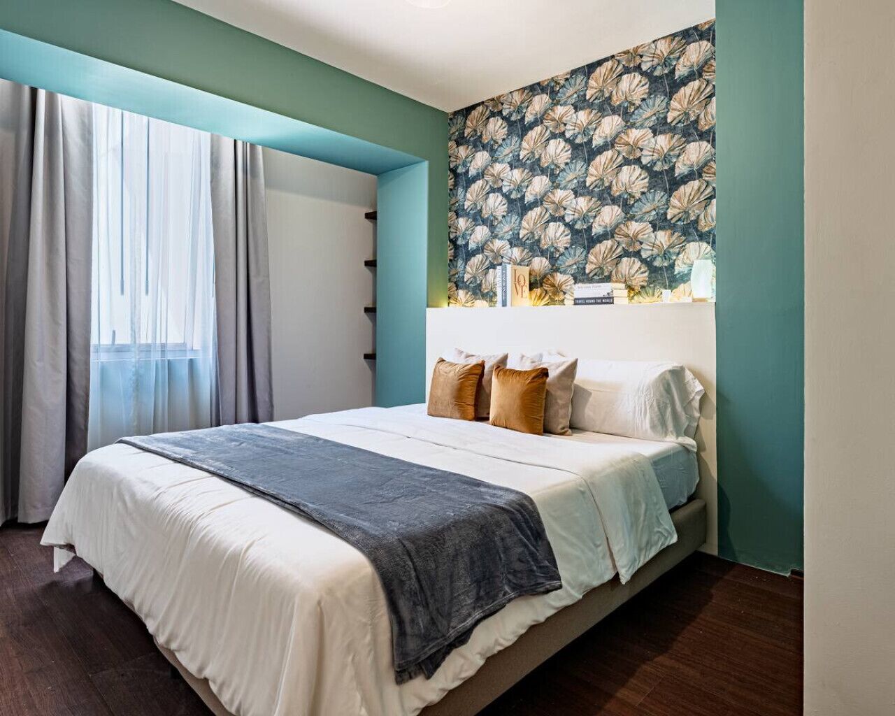 Ein Schlafzimmer mit einem Bett, Vorhängen, blumigem Wandpapier und einem Fenster.