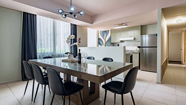 Un comedor moderno con una mesa de vidrio, sillas negras y una araña.