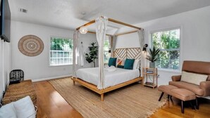 Ein Schlafzimmer mit Himmelbett, Holzboden, Wand-Fernseher und Fenster mit Jalousien.