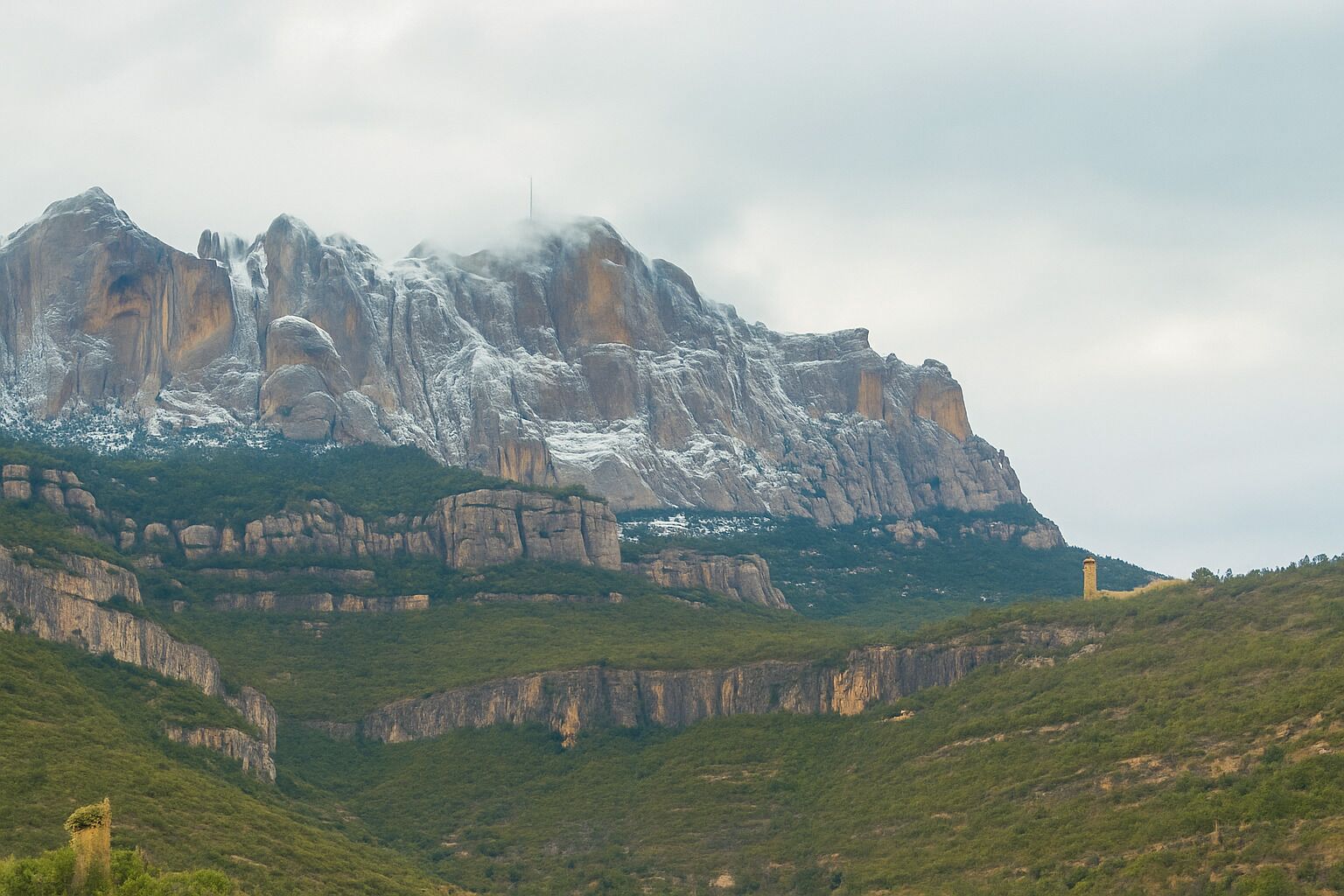Paesaggio montuoso con una roccia imponente e una piccola torre.
