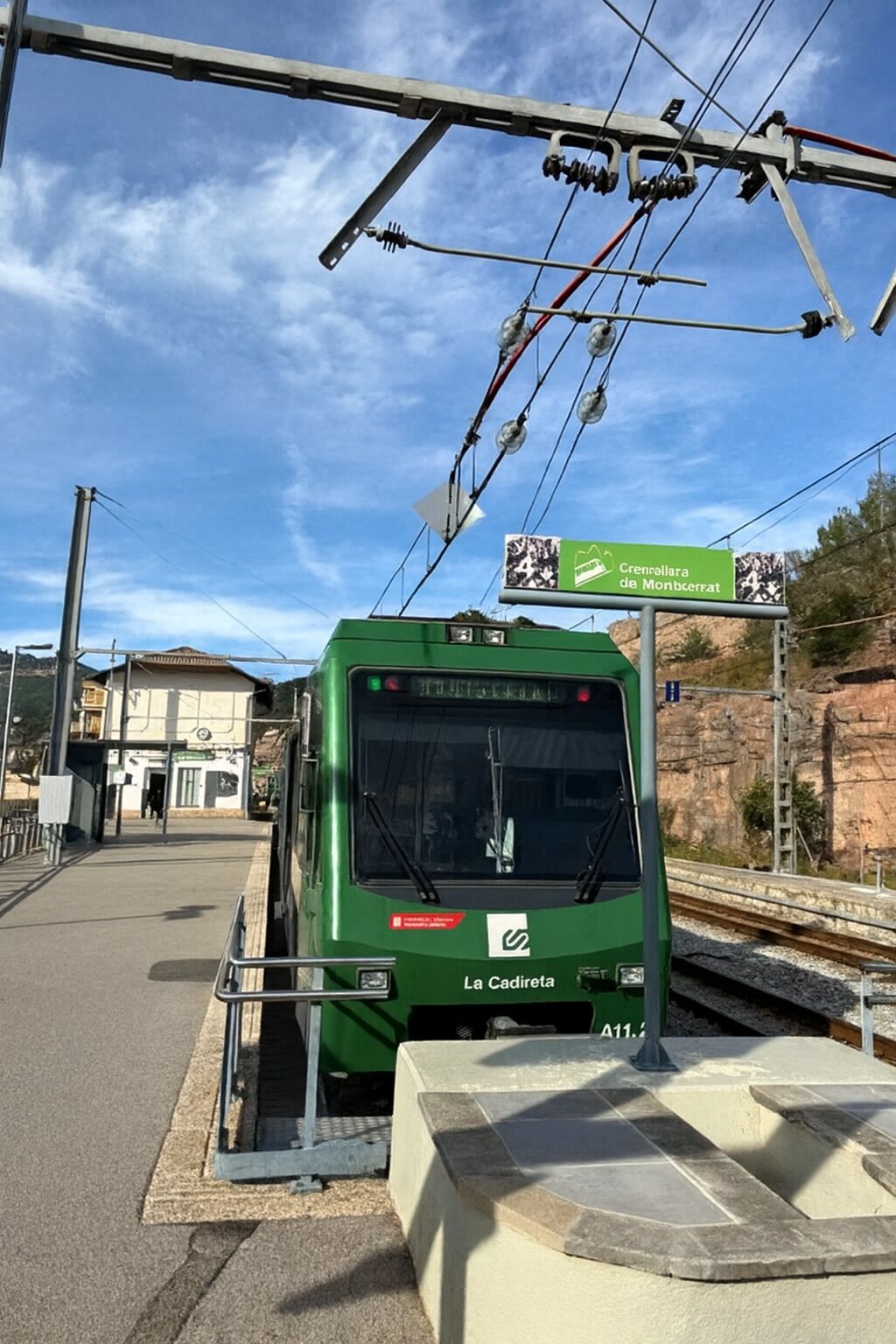 Un tranvía verde en una estación, con un cartel que indica 'Crénalha da Montserrat'.