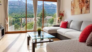 Una sala de estar moderna con una mesa de centro de vidrio, un sofá con cojines rojos y vistas a montañas a través de amplios ventanales.