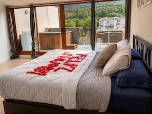 A bedroom with a large bed, a view of a balcony, and a cityscape in the background.