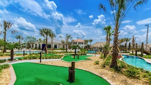 Un campo de mini golf con un área de putting verde, piscina y palmeras.