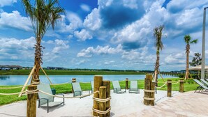 Un patio frente al agua con sillones de descanso y postes de madera, con vista a un lago y follaje.