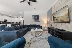 A modern living room with a sectional sofa, a coffee table, and a TV on a marble wall.