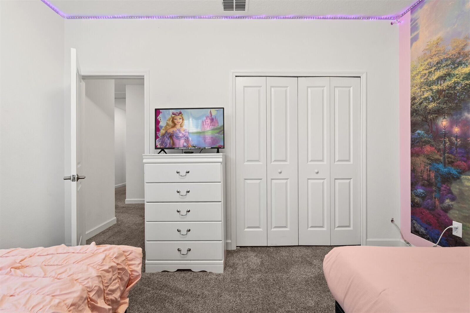 Een slaapkamer met een witte dressoir, een televisie erboven, een deur en een kleurrijke muurschildering.