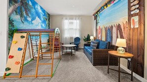 Habitación con pared de escalada, un sofá, una mesita y una pared decorada con tablas de surf.