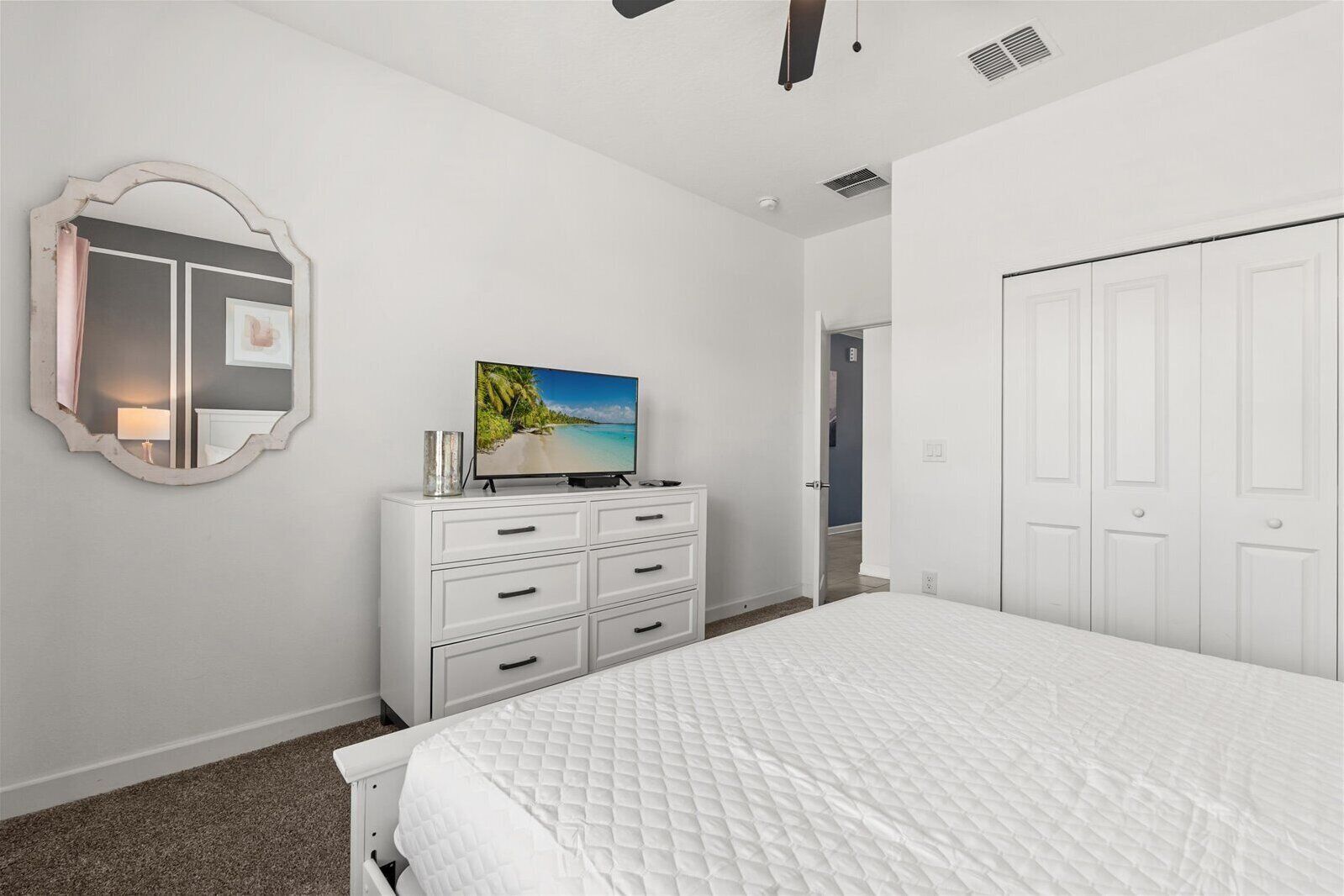 A bedroom with a bed, a dresser, a television displaying a beach scene, a mirror, and a door.