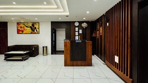 A modern reception area with a marble floor, a reception desk, a sofa, and a wall-mounted clock. - Hotel Ellora Inn Sultanpur (Sultanpur)