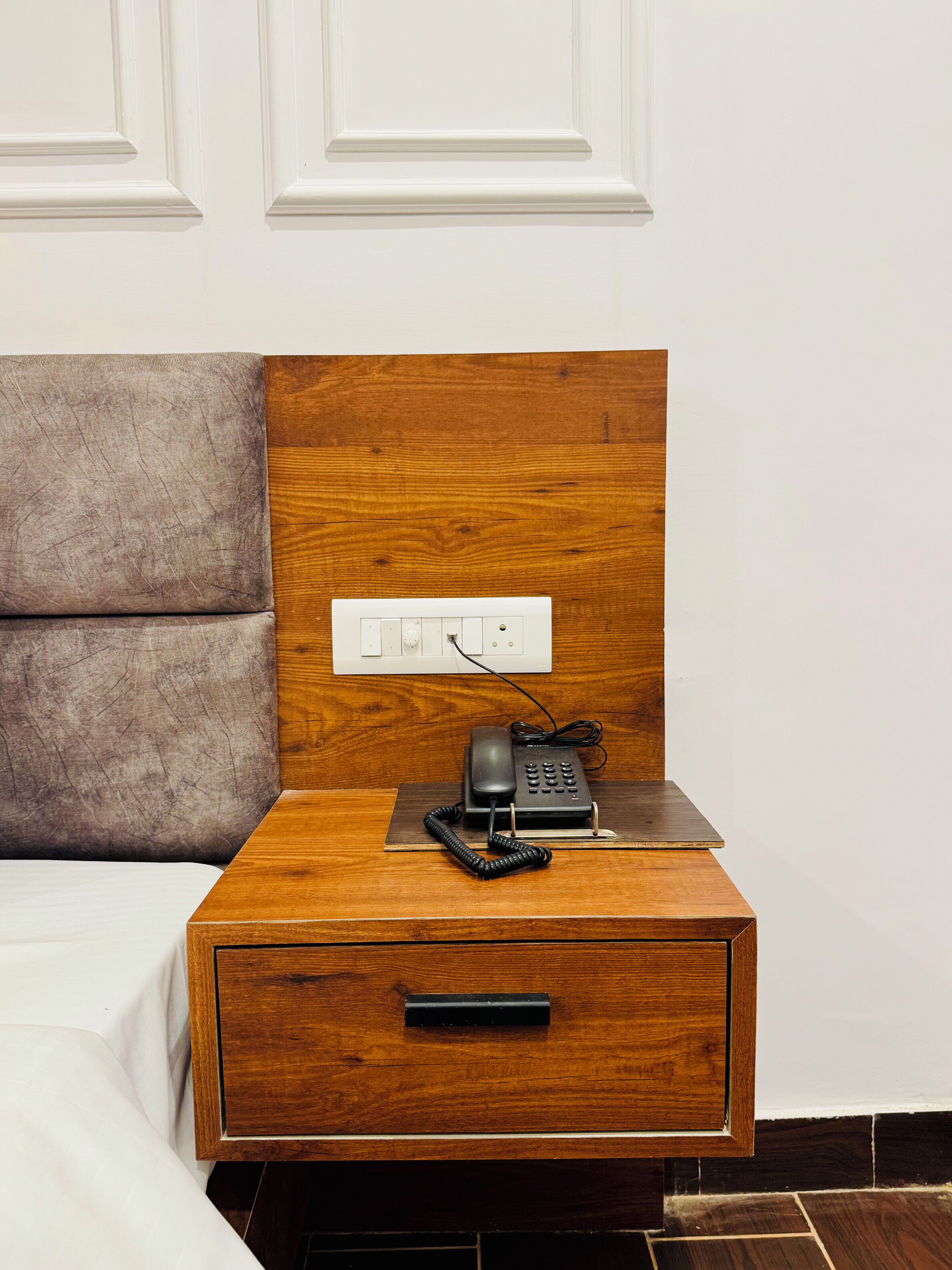Una mesita de noche de madera con un teléfono y un enchufe.