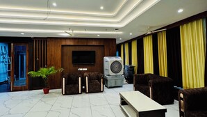A spacious living area with a flat-screen TV, comfortable seating, a large fan, and a ceiling fan. - Hotel Ellora Inn Sultanpur (Sultanpur)