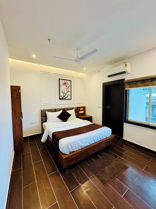A bedroom with a wooden bed, a ceiling fan, an air conditioning unit, and a window with a view. - Hotel Ellora Inn Sultanpur (Sultanpur)