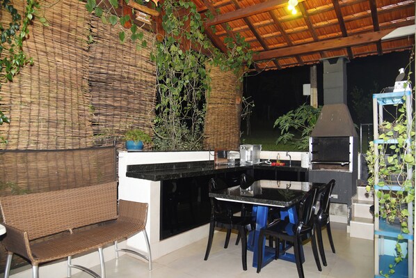 An outdoor kitchen area with a built-in grill, a dining table with chairs, and a bench.