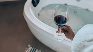 Una persona sosteniendo una copa de vino en un jacuzzi con vista a la vegetación.